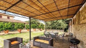 Eine Terrasse im Freien mit Korbmöbeln, einem Grill und Topfpflanzen.