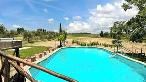 Ein rechteckiger Pool mit Holzterrasse und Blick auf einen Weinberg im Hintergrund.