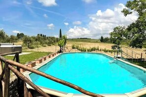 A rectangular swimming pool with a wooden deck and a view of a vineyard in the background. - Restored barn with views of Siena countryside (Castelnuovo Berardenga)
