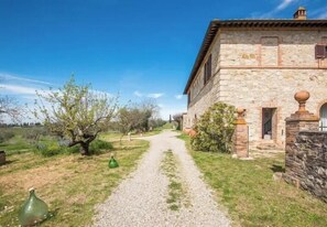 A stone building with a gravel path leading to it, surrounded by greenery and trees. - Restored barn with views of Siena countryside (Castelnuovo Berardenga)