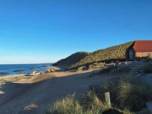 Ein Strand mit Booten, ein Gebäude mit rotem Dach und ein grasbewachsener Hügel.