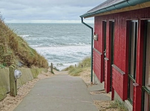 Ein Küstenweg führt zu einem roten Gebäude mit Blick aufs Meer.