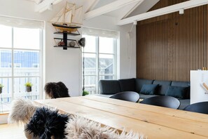 Ein modernes Wohnzimmer mit einem Holztisch, einem dunkelgrauen Sofa und einem Schiffsmodell an der Wand.