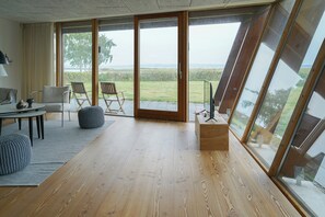 Une pièce moderne avec un plancher en bois, un canapé, une table et des chaises. De grandes fenêtres offrent une vue sur l’extérieur.