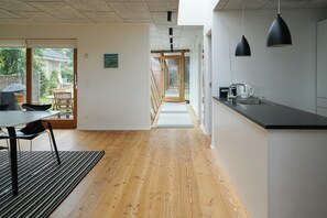 A modern kitchen with a wooden floor, a dining area with a table and chairs, and a view through an open door to a garden. - View over Aarhus bay from striking architecture (Egå)