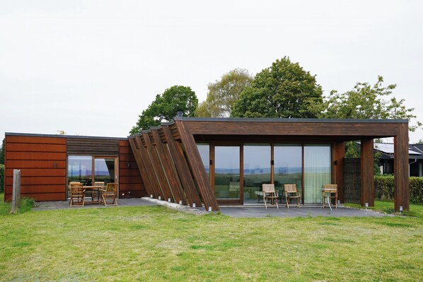 A modern house with a sloped roof, large glass windows, and a patio with outdoor furniture. - View over Aarhus bay from striking architecture (Egå)