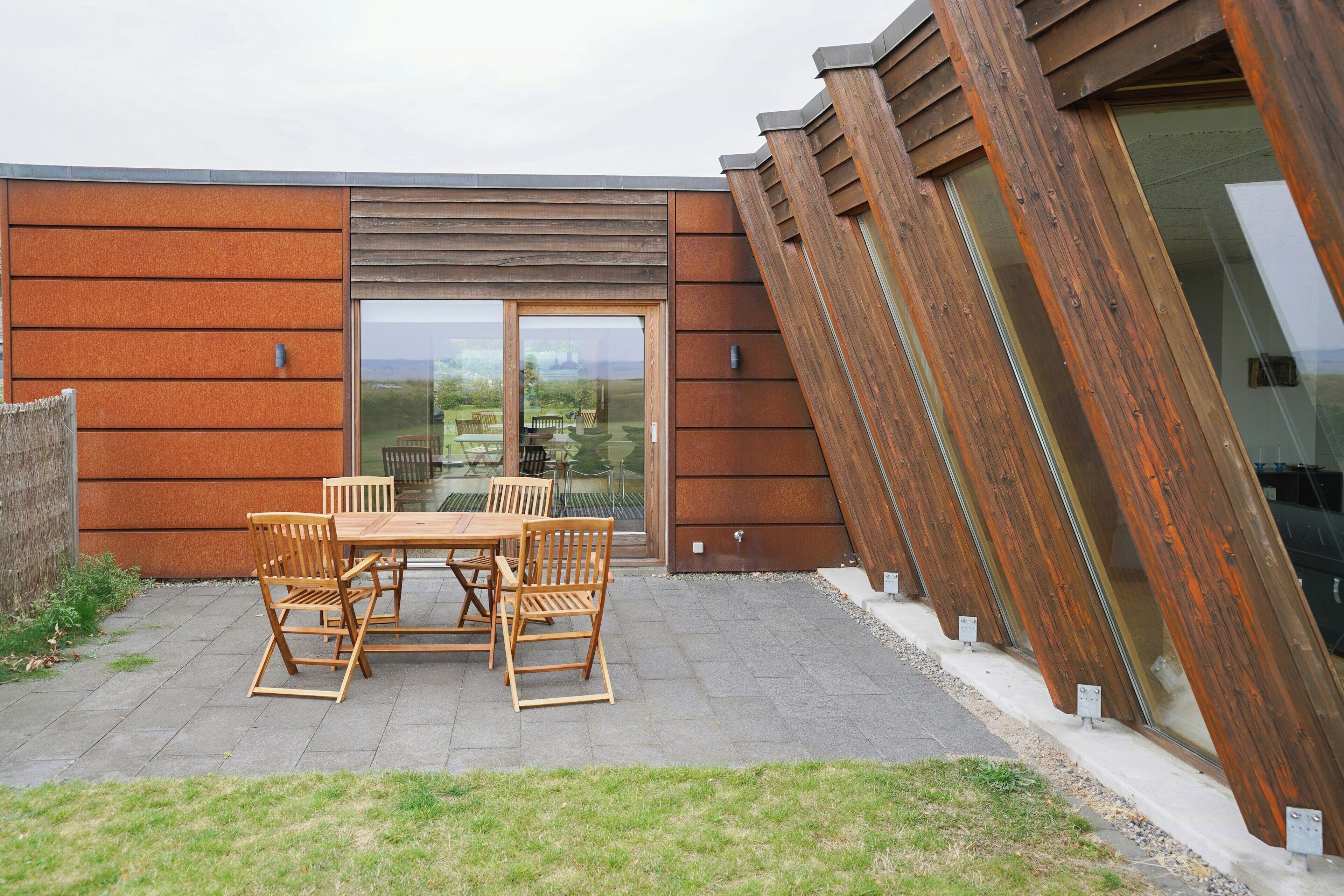 Een terras met een tafel, stoelen, een glazen deur en een houten omheining.