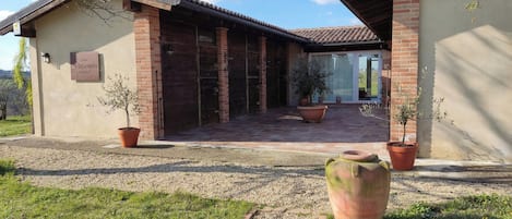 A building with a brick facade, a tiled roof, and a gravel driveway. There are potted plants and a large terracotta pot in the foreground.