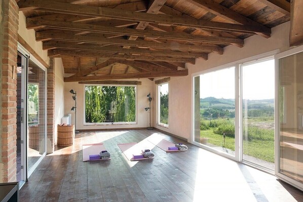 Ein geräumiges Zimmer mit Holzbalkendecke, großen Fenstern und Yogamatten auf dem Boden.