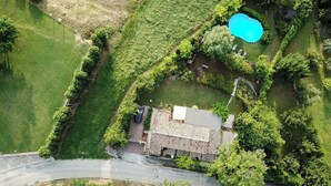 Et luftfoto af et hus med swimmingpool, omgivet af grøn vegetation og en belagt indkørsel.