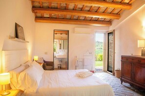 A bedroom with a bed, bedside lamps, a wooden headboard, a mirror, a bathroom with a sink, and a view of the outdoors. - Villa with views of Ostra and Marche countryside (Ostra)