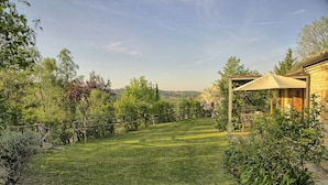 En græsplæde med træhegn, en pergola med markise og en bygning med tegltag.