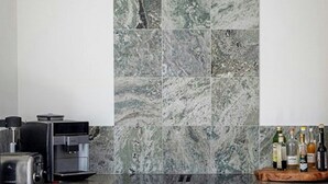 A modern kitchen with a marble backsplash, wooden cabinets, and a coffee machine.