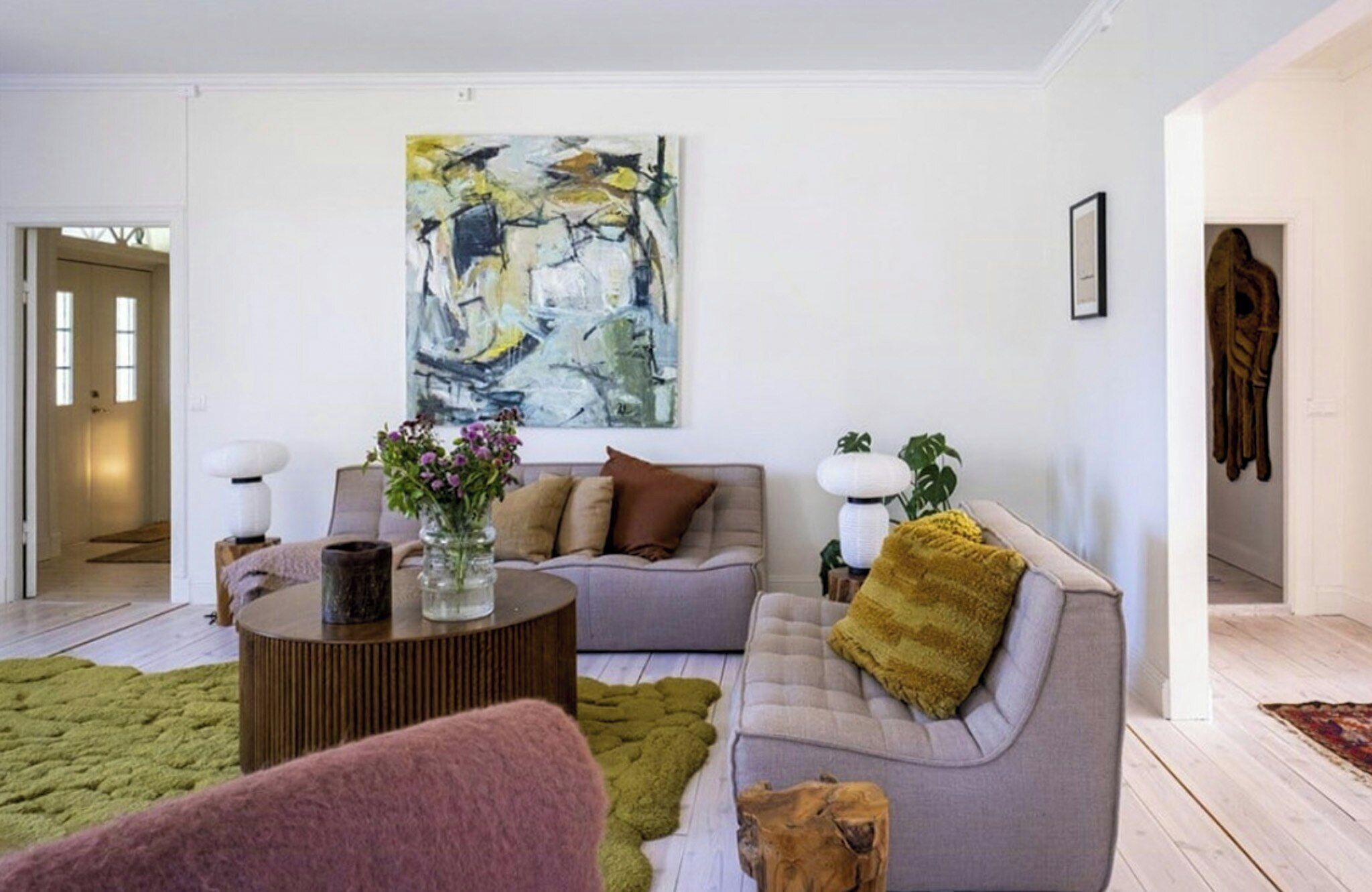Een moderne woonkamer met een grijze bank, een salontafel en een groot abstract schilderij aan de muur.
