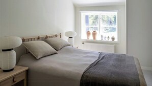 A bedroom with a bed, bedside lamp, and a window with vases.