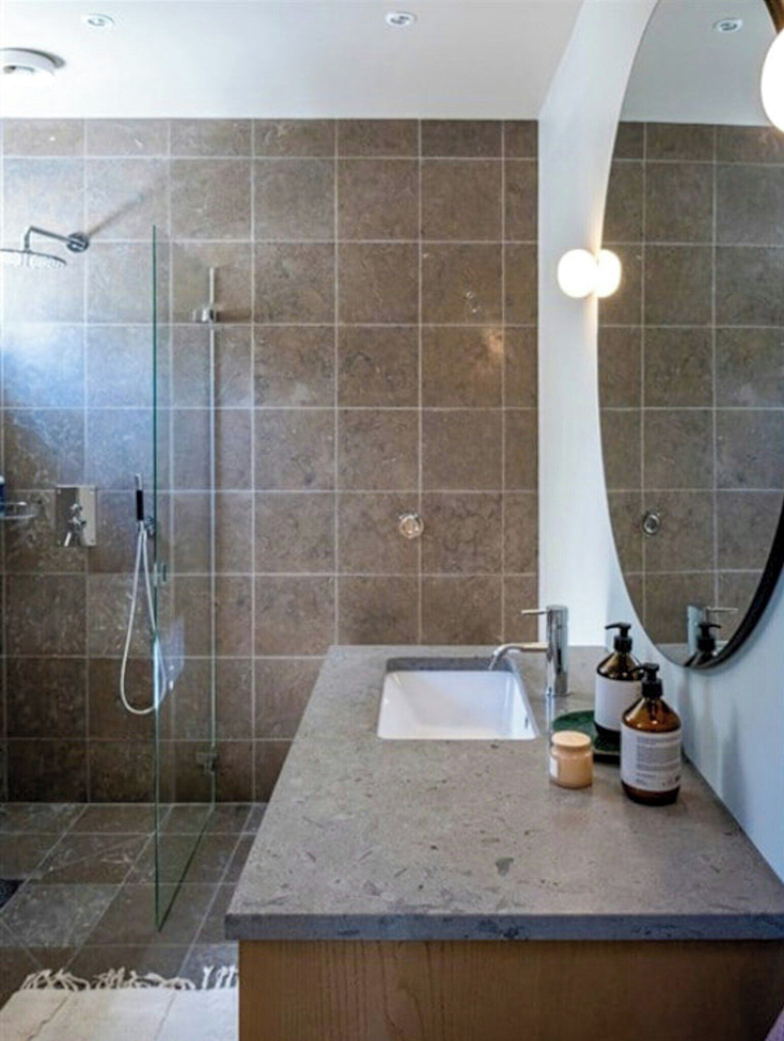 Un bany modern amb una cabina de dutxa de vidre, un lavabo amb mirall i productes de tocador a la superfície.