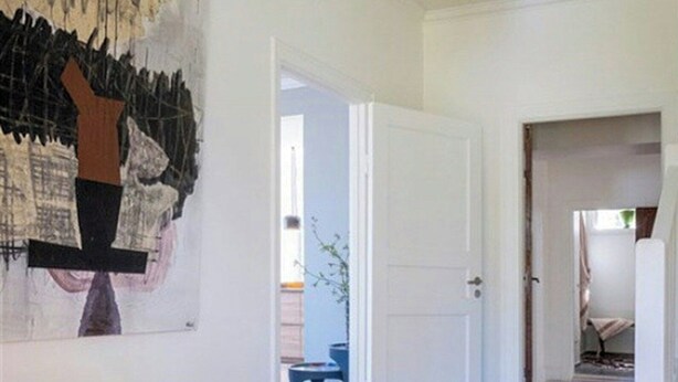 A modern interior with a large abstract painting, a dining area with a table and chairs, and a hallway leading to another room.