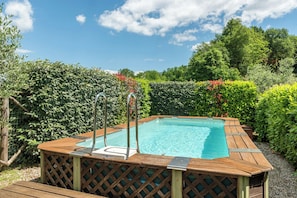 Ein rechteckiges Whirlpool mit Holzterrasse und Metallleiter, umgeben von üppiger Vegetation und Bäumen.