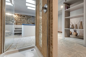 Ein Badezimmer mit Badewanne, einer Duschkabine aus Glas, einer Steinwand und einem weißen Regal mit Dekoration.