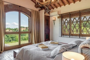 Ein Schlafzimmer mit großem Fenster, einem Bett, einem Nachttisch und einer Lampe.