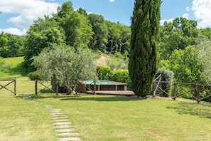 Ein Poolbereich mit Holzterrasse, umgeben von üppiger Vegetation und Bäumen.