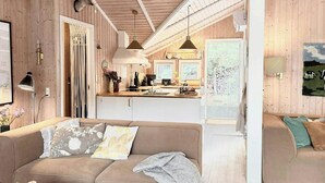 A cozy living room with a sofa, a chessboard, and a kitchen in the background. - House in the heather with sea view on Odden (Sjællands Odde)
