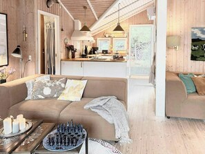 A cozy living room with a sofa, a chessboard, and a kitchen in the background. - House in the heather with sea view on Odden (Sjællands Odde)