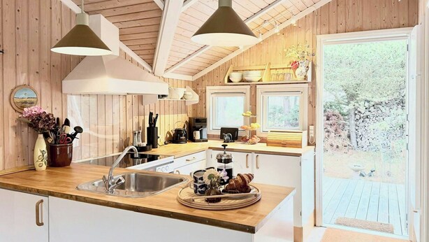 A kitchen with wooden walls, a sink, and a window overlooking a garden. - House in the heather with sea view on Odden (Sjællands Odde)