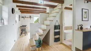 Una escalera de madera con peldaños y una planta colgante, que conduce a una habitación con pared blanca y un cuadro enmarcado.