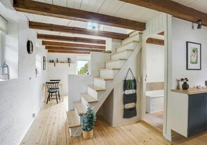 Una escalera de madera con peldaños y una planta colgante, que conduce a una habitación con pared blanca y un cuadro enmarcado.