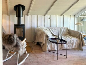 Ein gemütliches Zimmer mit einem weißen Schaukelstuhl, einem Sofa mit kuscheliger Decke und einem Tisch mit Kerzen.