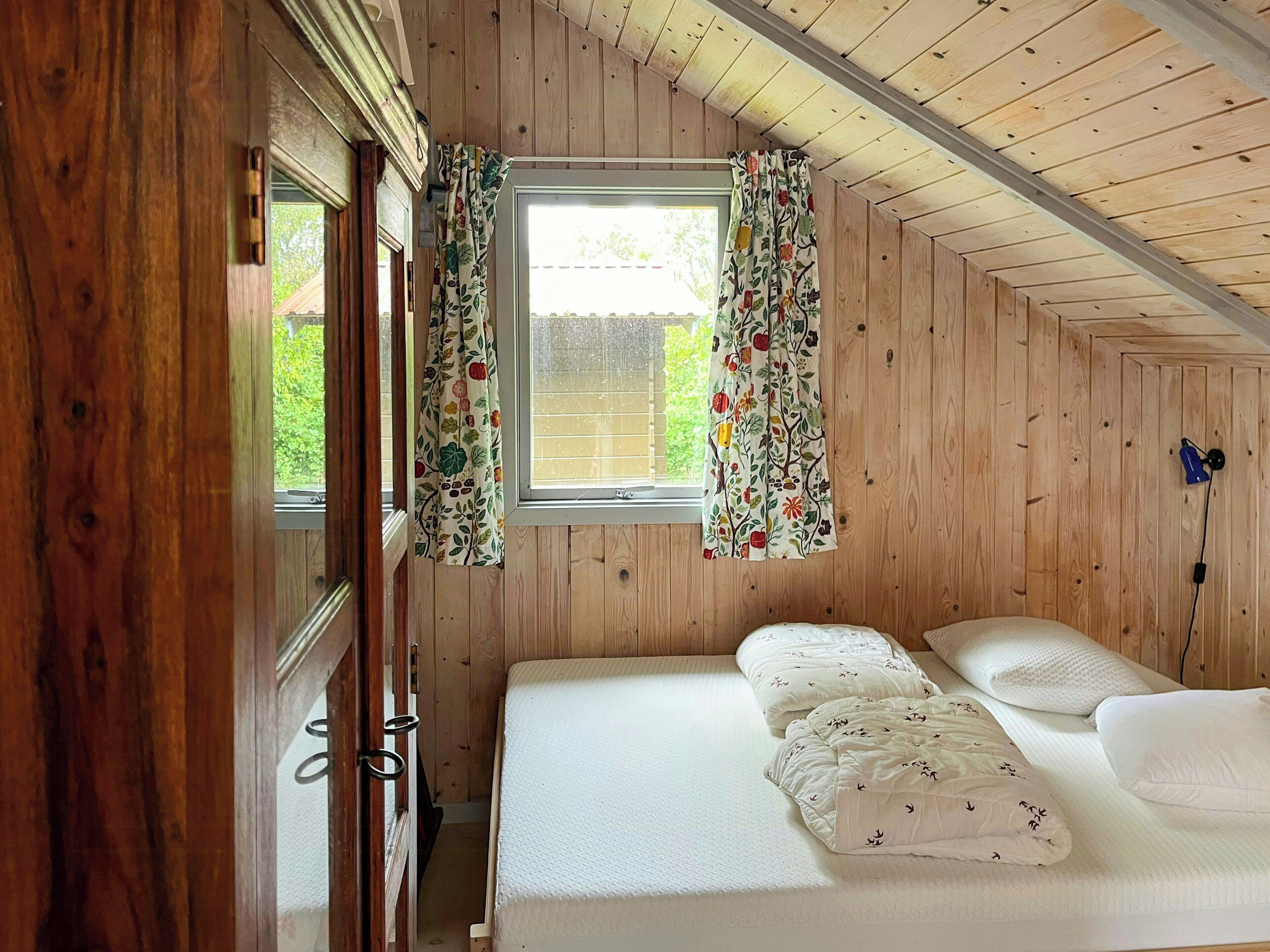 A wooden-paneled room with a bed, curtains, and a window.