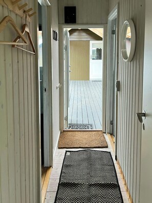 Ein Flur mit Holzboden, einem schwarz-weißen Teppich, einer Holztür und einem an der Wand befestigten Spiegel.