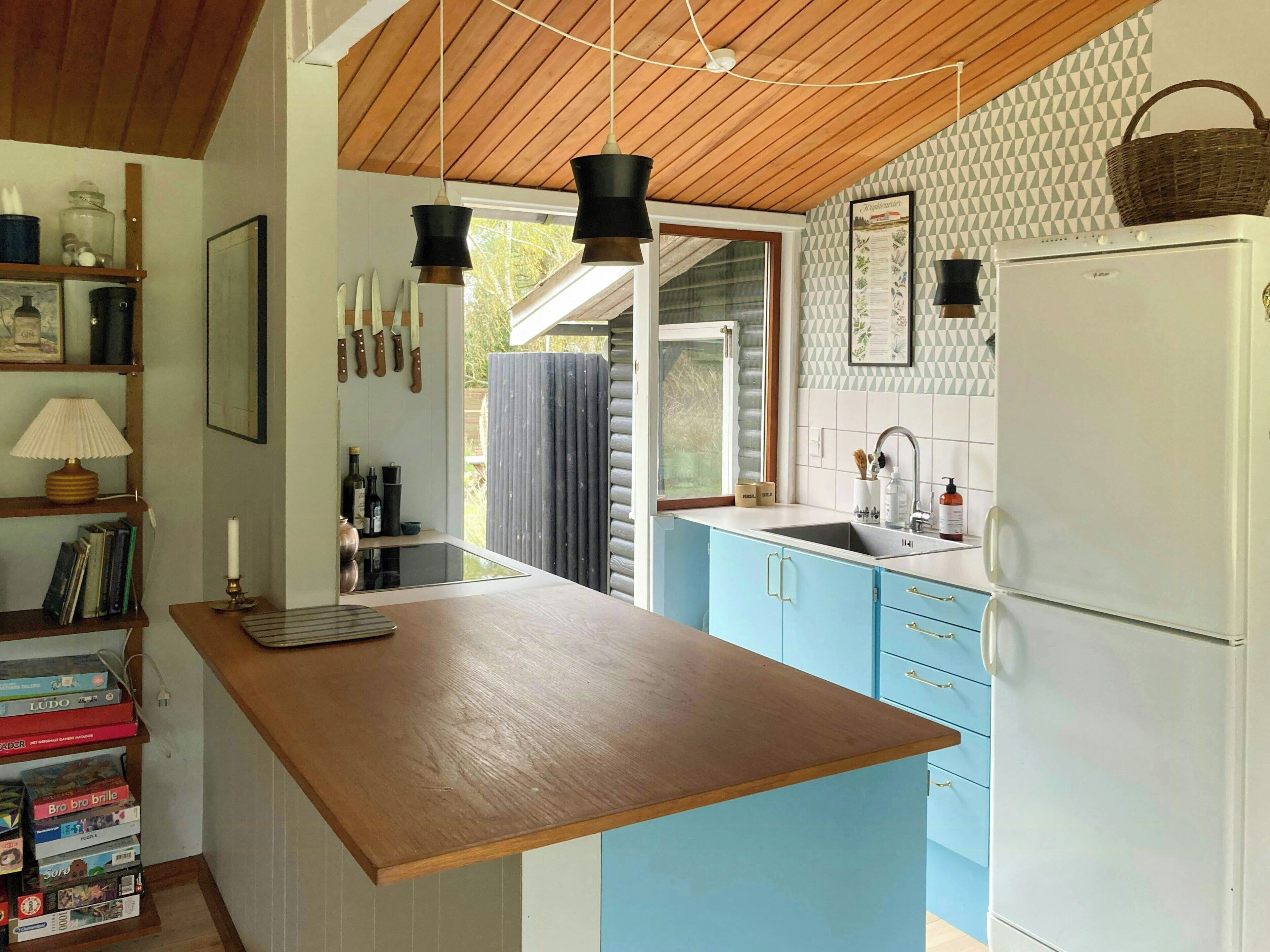 Une cuisine avec un plafond en bois, un réfrigérateur blanc, des armoires bleues et un plan de travail en bois.
