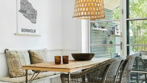 Un intérieur moderne avec un plafond blanc, une table en bois sur laquelle se trouvent un saladier et des verres, des chaises en osier et un luminaire suspendu.
