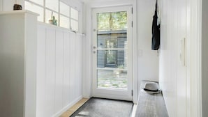 Une porte blanche avec un panneau de verre, un banc en bois et un sac noir accroché au mur.