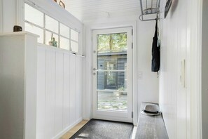 Eine weiße Tür mit Fensterglas, eine hölzerne Bank und eine schwarze Tasche an der Wand hängend.