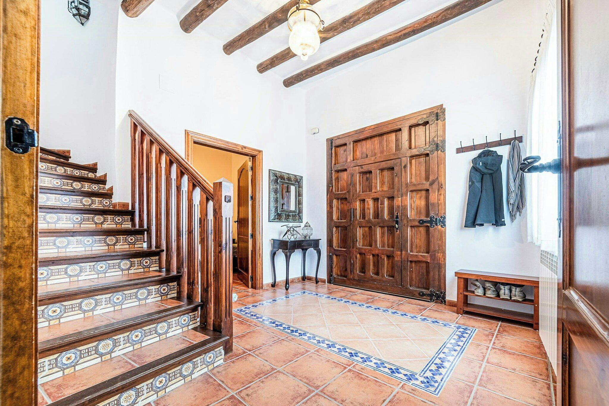 Una escala amb rajoles estampades, una porta de fusta i un penjador amb jaquetes.