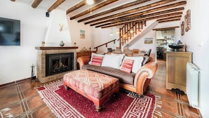 Una sala de estar acogedora con vigas de madera a la vista, chimenea, sofá con cojines estampados y alfombra roja.