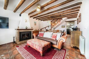 Un soggiorno accogliente con travi a vista in legno, un caminetto, un divano con cuscini decorati e un tappeto rosso.