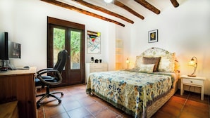 Un dormitorio con cama, escritorio, silla, televisión y puerta que da a un balcón.