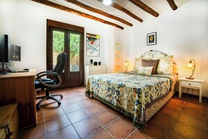 Una camera da letto con un letto, una scrivania, una sedia, una televisione e una porta che dà su un balcone.