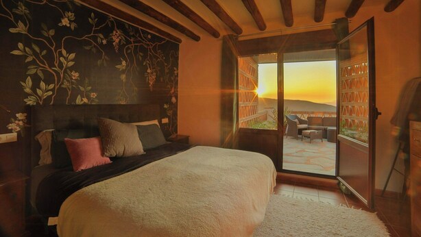 Un dormitorio con una cama grande, vistas al exterior a través de una puerta corredera y un techo con vigas a la vista.