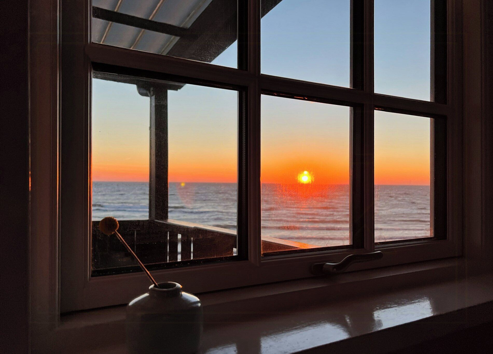 A window with a view of the ocean at sunset.