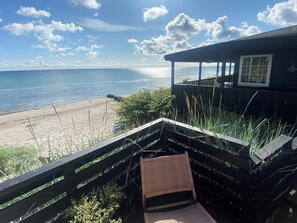A beach view from a wooden deck with a chair and a table, overlooking the ocean.