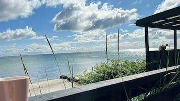 A beach view with a wooden deck, a cup on the railing, and a clear sky.