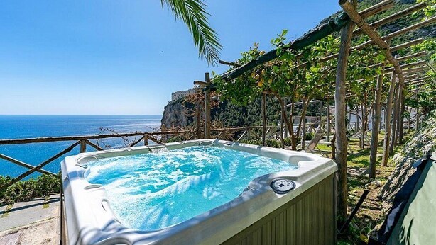 A hot tub with a view of the sea, surrounded by wooden structures and greenery.