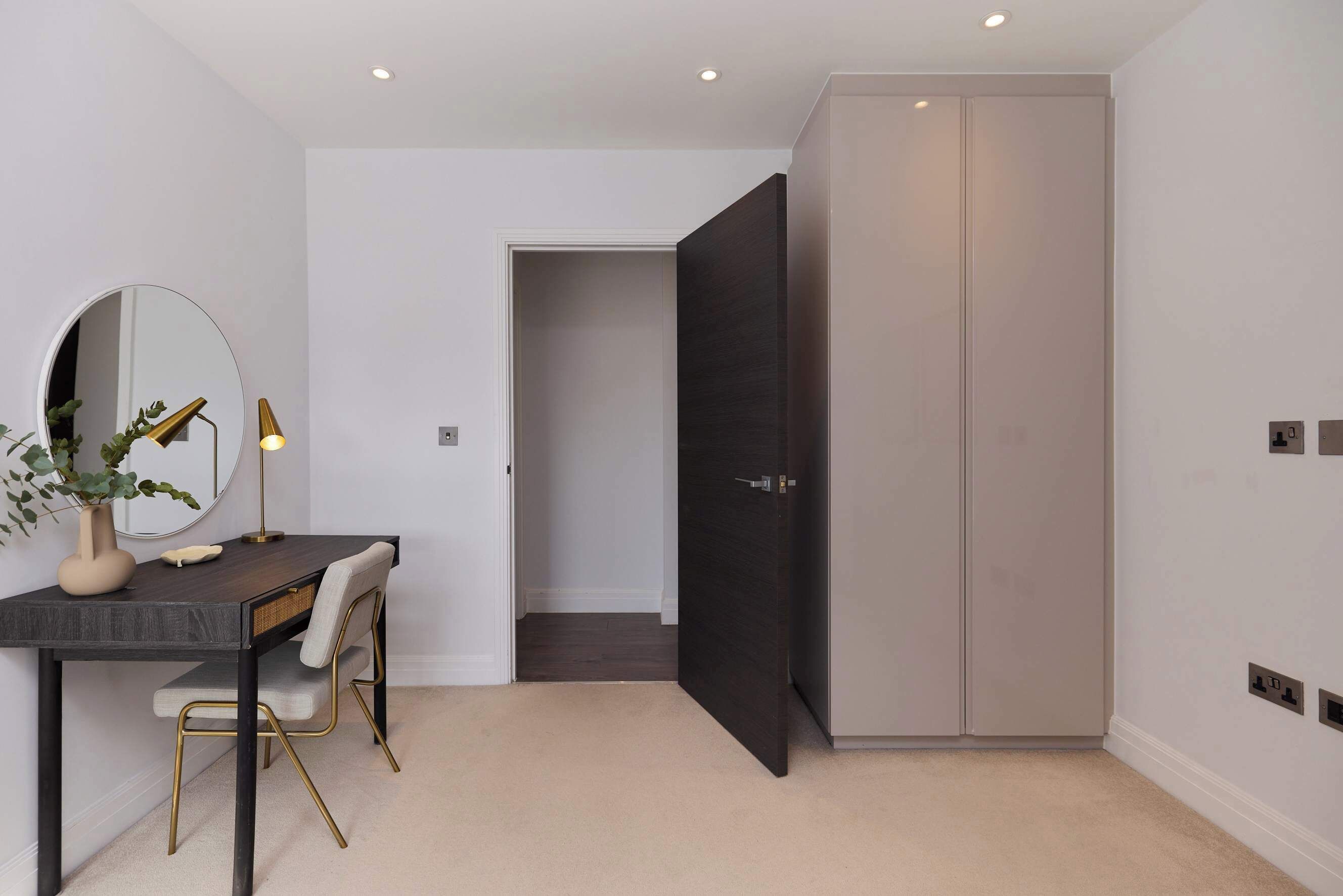 A modern room with a desk, chair, mirror, and wardrobe.