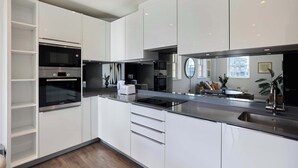 Eine moderne Küche mit weißen Schränken, einem eingebauten Backofen, einer Edelstahlspüle und einem großen Fenster.