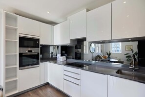 Eine moderne Küche mit weißen Schränken, einem eingebauten Backofen, einer Edelstahlspüle und einem großen Fenster.